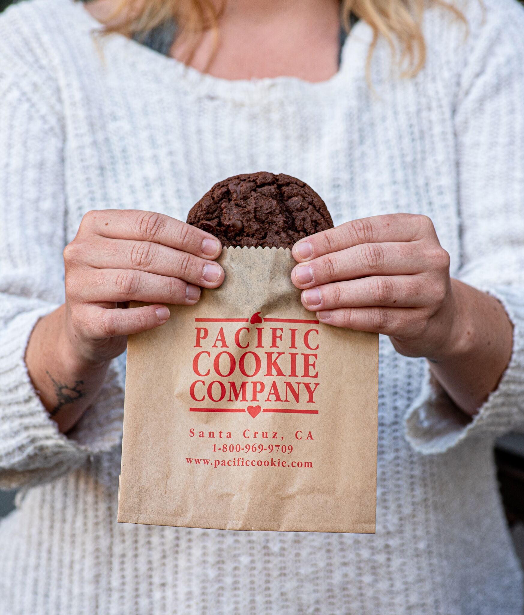 A woman holding a Dr. Midnight chocolate cookie in a Pacific Cookie Company bag