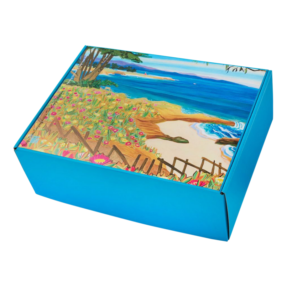 West Cliff Cookie Gift Box - A blue gift box with painting Out Front by local artist Tessa Hope Hasty, featuring a scenic coastal view of sand, surf, wildflowers, and cypress trees along the Monterey Bay shoreline.