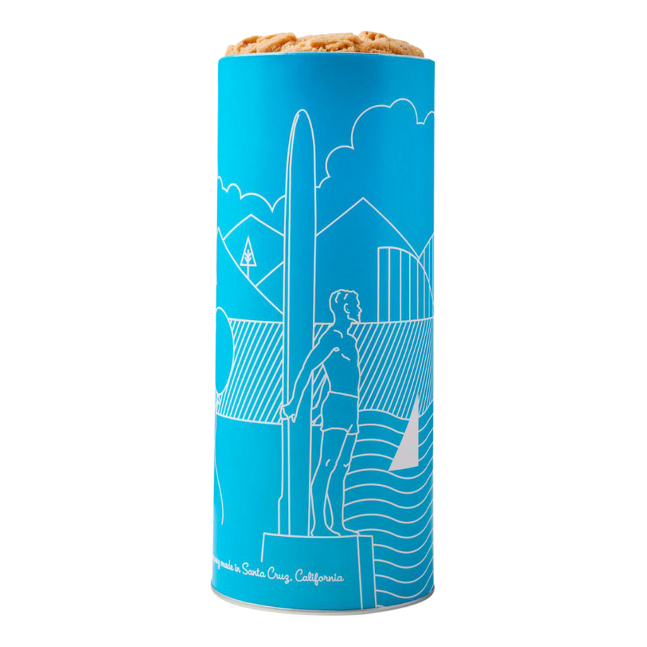 A vibrant blue design featuring a white line illustration of the iconic surfer statue in Santa Cruz, California. The tin is filled with fresh-baked cookies visible at the top.