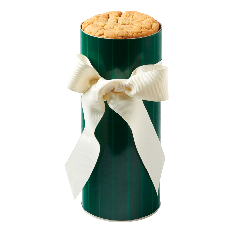 Green cylindrical cookie gift tin filled with fresh-baked cookies and wrapped with a white ribbon tied in a bow.